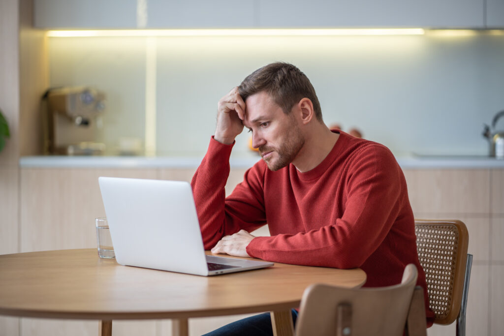 Mann sitzt am Laptop und denkt nach